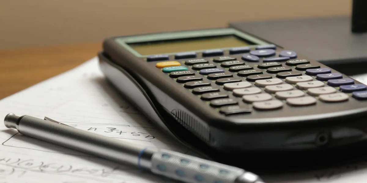 Taschenrechner und Stift liegen auf einem Heft voll mit mathematischen Formeln.