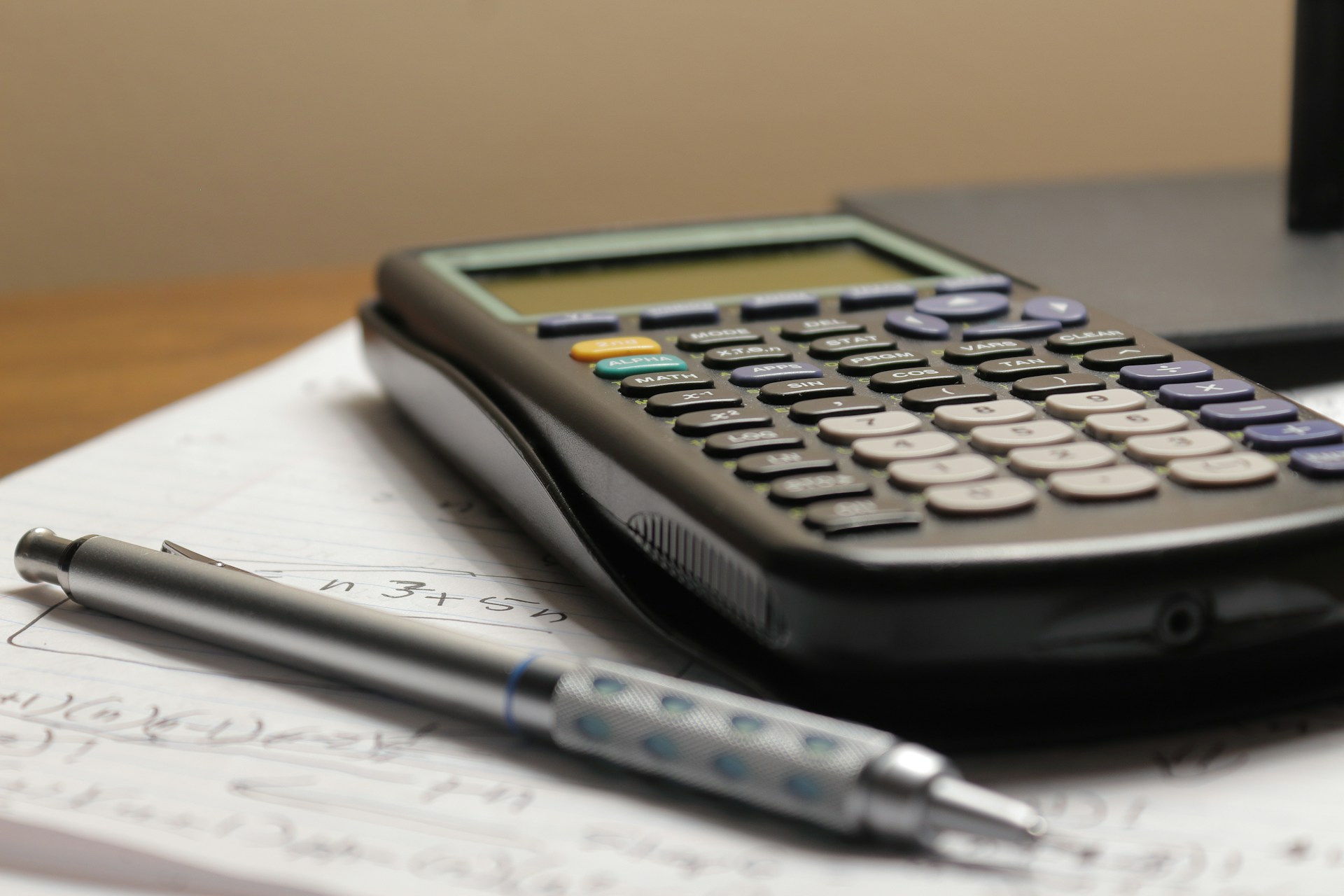 Taschenrechner und Stift liegen auf einem Heft voll mit mathematischen Formeln.
