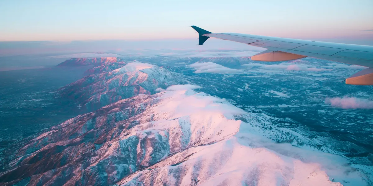 Blick aus einem Flugzeugfenster. Man sieht eine Schneebedeckte Berglandschaft und das Ende des Flugzeugfl&uuml;gels.