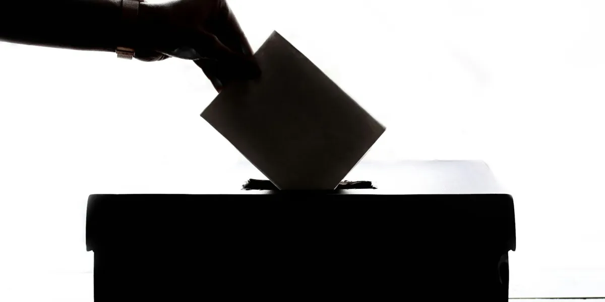 Ein Kuvert wird in eine Wahlurne geworfen.