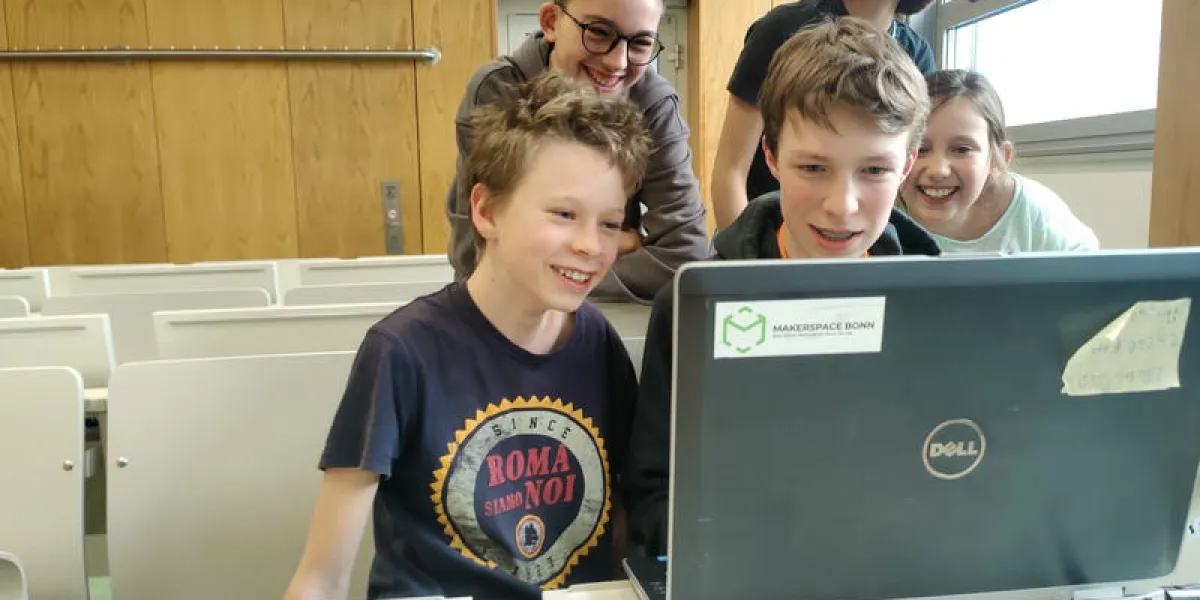 Mehrere Kinder lachen hinter einem Laptop, an dem sie ein Spiel ausprobieren.