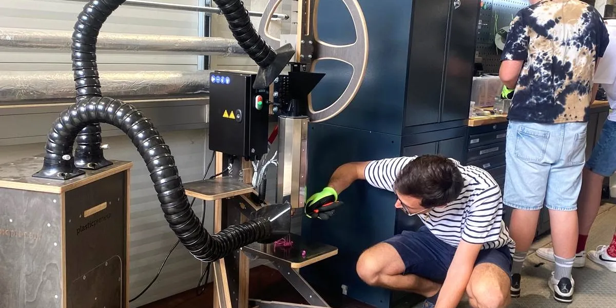 Man sieht eine gro&szlig;e Spritzgussmaschine. Ein Mann arbeitet gerade mit einem Schraubezieher daran.