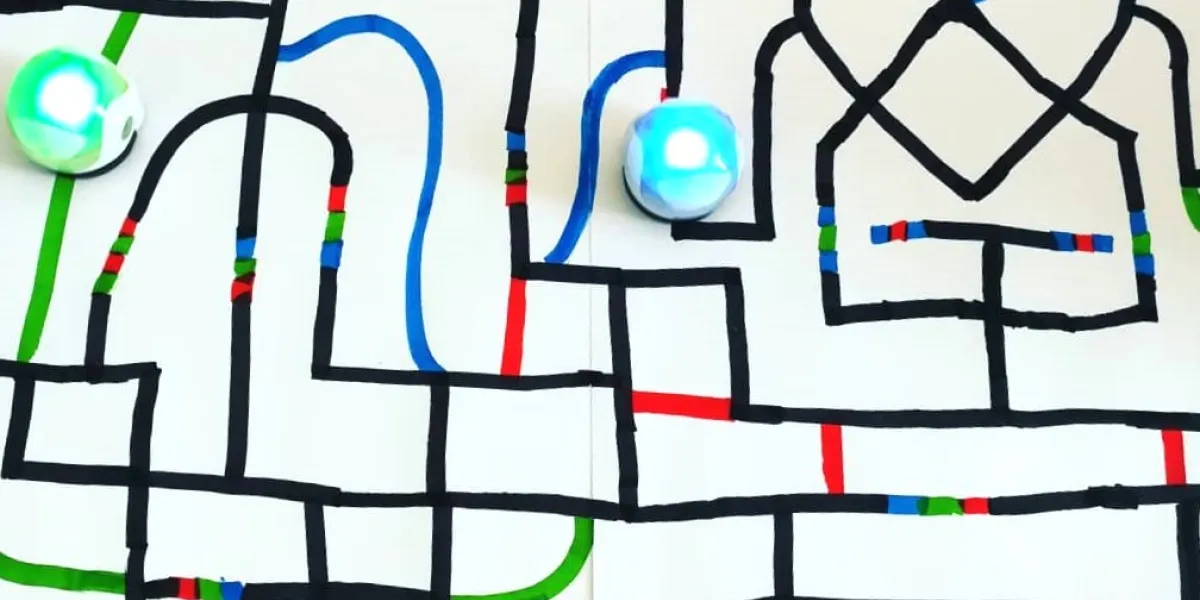Ein gro&szlig;es Blatt Papier mit lauter bunten Bahnen. Zwei Ozobots (kleine runde Roboter) fahren entlang der Bahnen. Einer leuchtet gr&uuml;n, der andere blau.