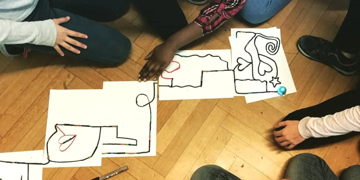 Sch&uuml;ler*innen sitzen rund um gezeichnete Ozobot-Strecke.