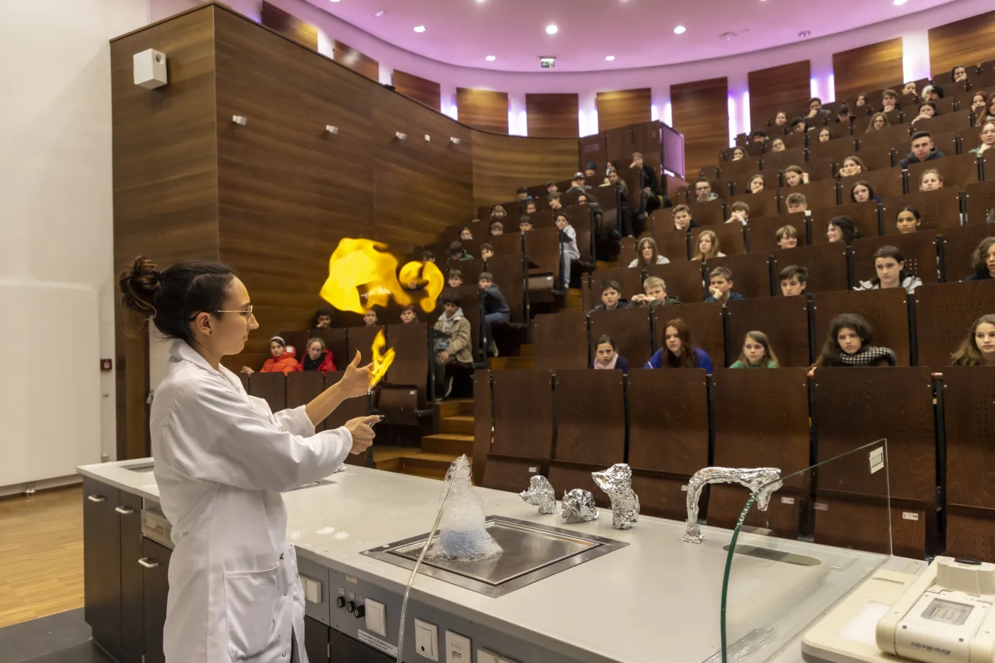 Ein Chemie-Experiment mit Feuer! Eine Chemikerin steht im Vorlesungssaal. In ihren H&auml;nden lodern Flammen.