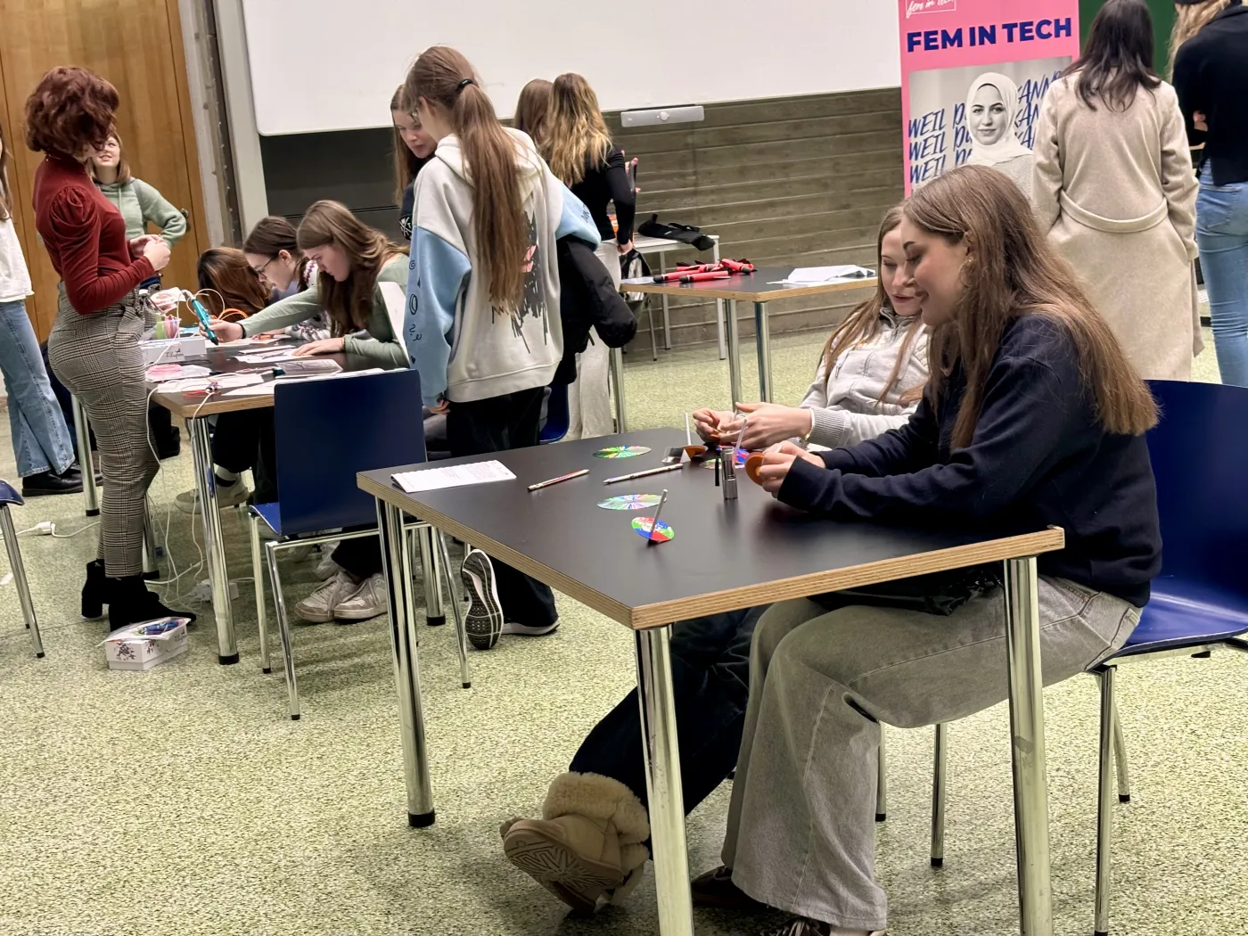 Hands-on-Aktivit&auml;ten am FIT-Infotag 2025. Sch&uuml;ler*innen stehen und sitzen an 2 Tischen und versuchen sich an den Aufgabenstellungen.