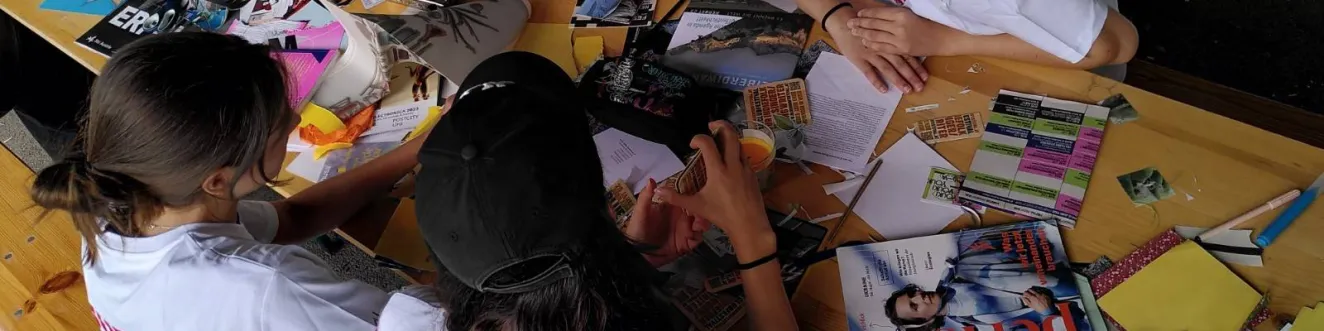 Vier Teilnehmer*innen sitzen an einem Biertisch, der mit Flyern, Magazinen und Stickern bedeckt ist. Alle tragen wei&szlig;e T-Shirts, auf denen "Super Science Team" steht.