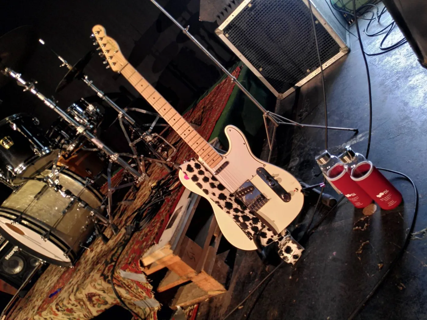 Eine wei&szlig;e E-Gitarre steht vor einer B&uuml;hne. Vor der Gitarre stehen zwei Flaschen mit der Aufschrift "TU Graz".