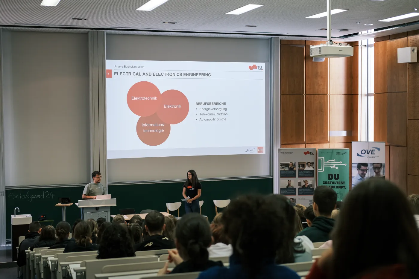Ansicht aus dem Publikum vom GEED 2024. Auf der B&uuml;hne pr&auml;sentieren 2 Studierende die Berufsm&ouml;glichkeiten nach dem Studium.