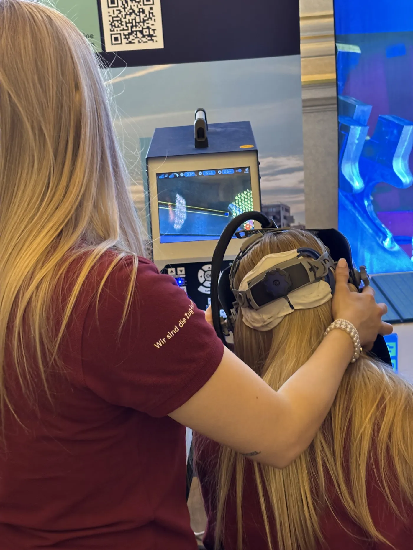 Das VR-Schwei&szlig;erlebnis aus einer anderen Perspektive: Man sieht das M&auml;dchen von hinten. Ihr wird gerade die VR-Brille aufgesetzt.