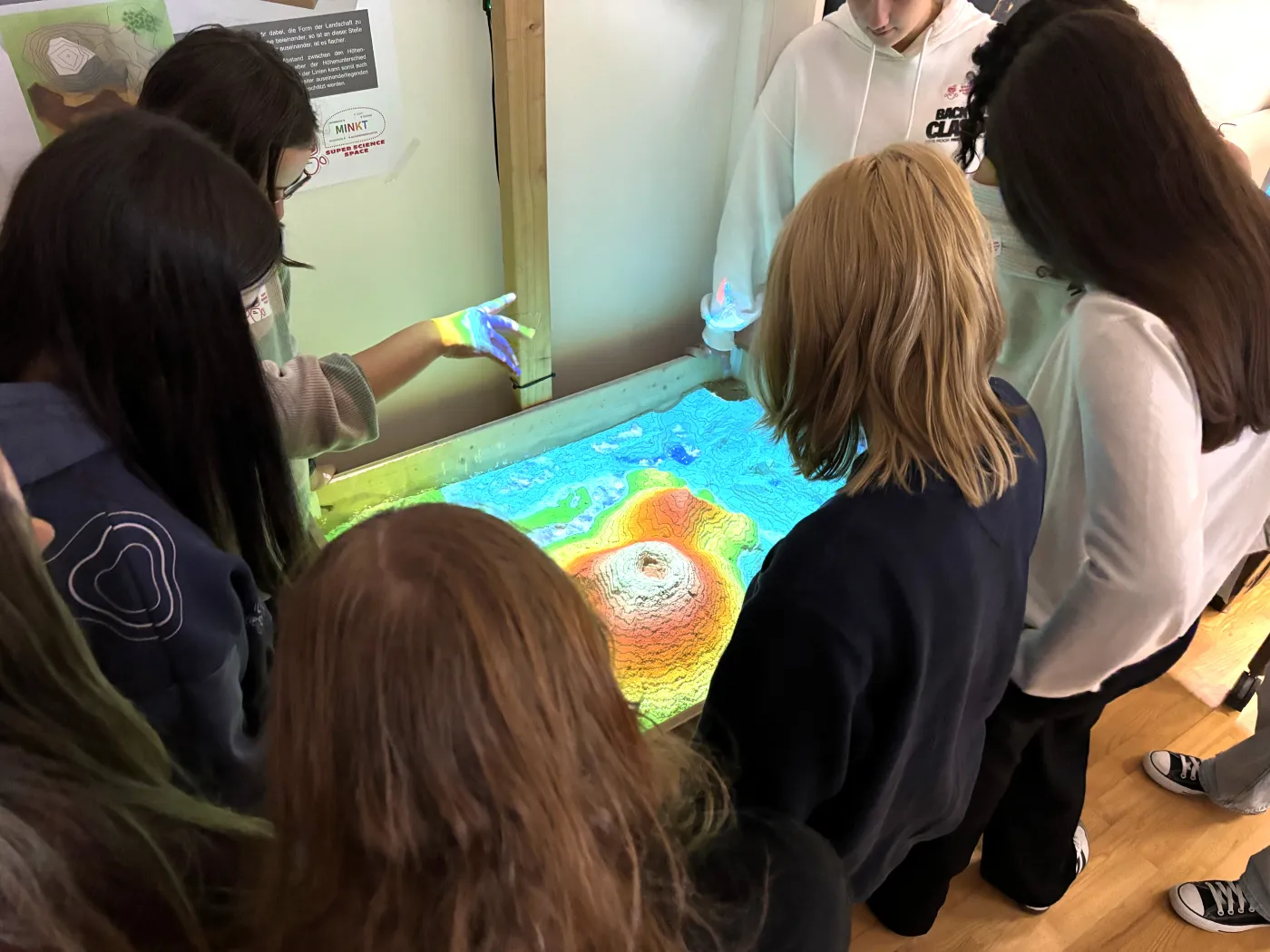 Die AR-Sandbox. Sch&uuml;lerinnen spielen mit der Projektion auf dem Sand.
