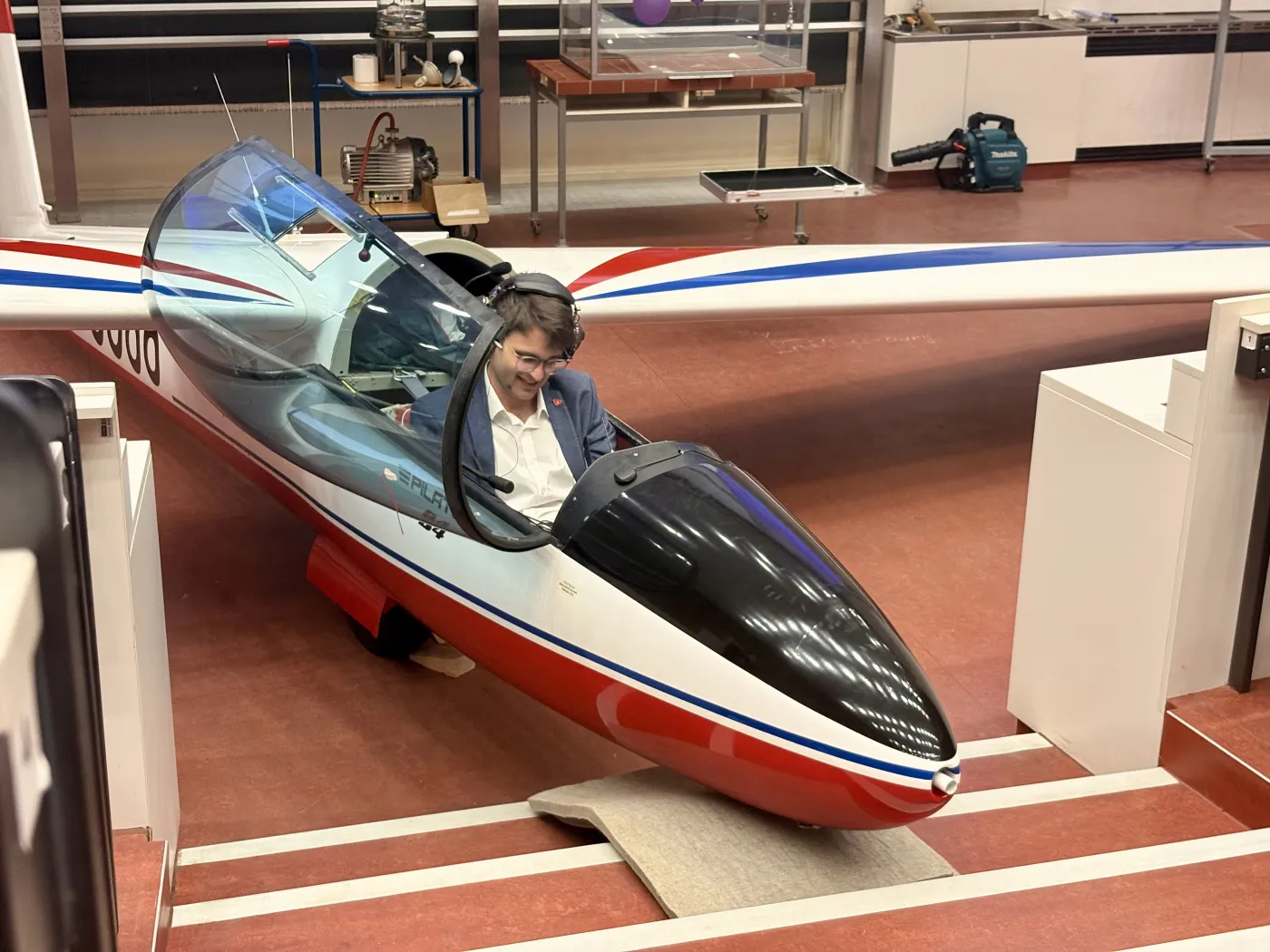 Ein Mann mit dunklen kurzen Haaren sitzt im Cockpit eines Segelflugzeuges. Die Glasabdeckung ist ge&ouml;ffnet.