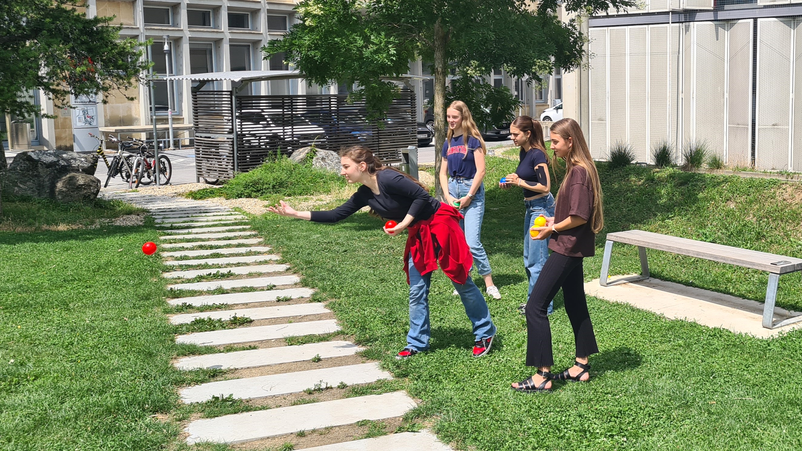 Vier Workshopteilnehmerinnen beim Bocciaspielen. Eines der M&auml;dchen wirft gerade einen roten Ball. Die anderen beobachten gespannt.
