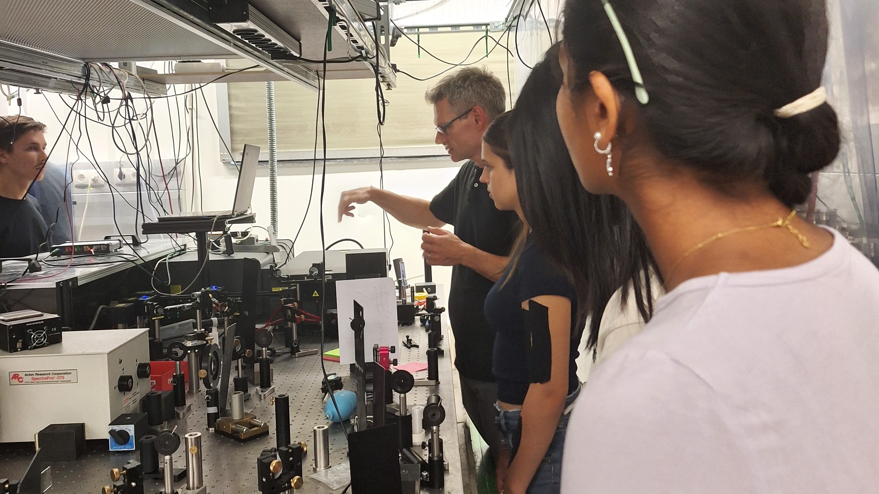 Ausflug ins Labor: Die Workshopteilnehmer*innen stehen in einem Labor. Am Tisch vor ihnen stehen viele wissenschaftliche Aparaturen; von der Decke h&auml;ngen Kabel.