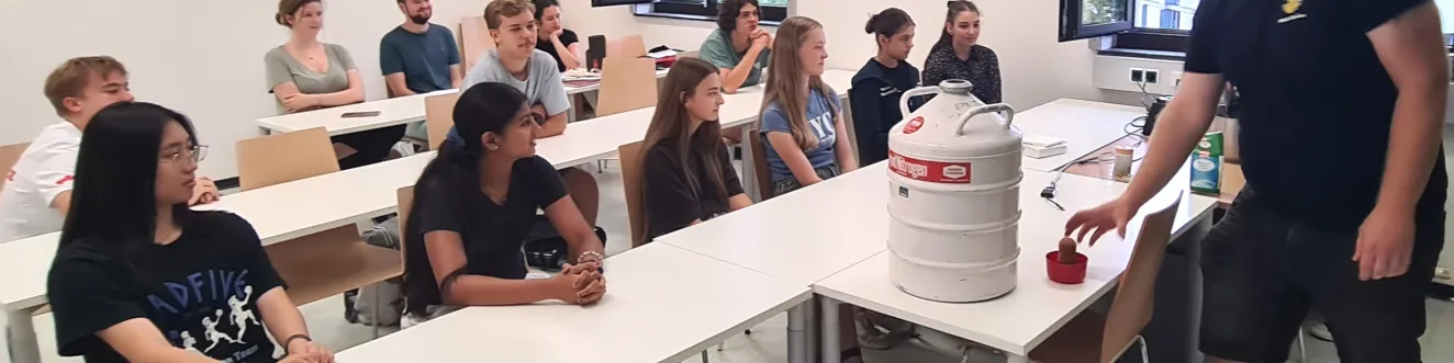 Workshopteilnehmer*innen beobachten einen Lehrer bei einem Experiment mit fl&uuml;ssigem Stickstoff.