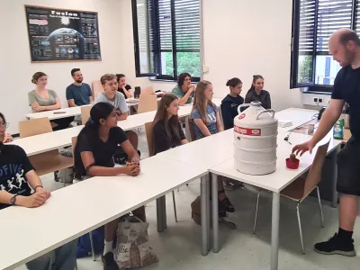 Workshopteilnehmer*innen beobachten einen Lehrer bei einem Experiment mit fl&uuml;ssigem Stickstoff.