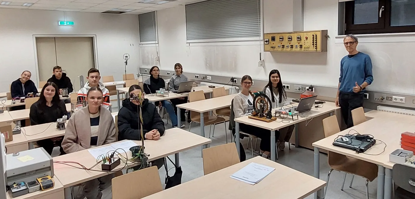 Sch&uuml;ler*innen sitzen an ihren Tischen mit Experimenten und l&auml;cheln in die Kamera.
