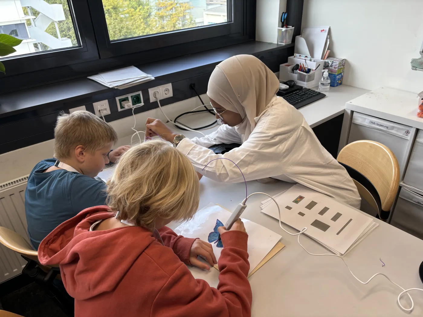 Eine Betreuerin vom Super Science Team zeigt zwei Buben wie man einen 3D-Stift verwendet.