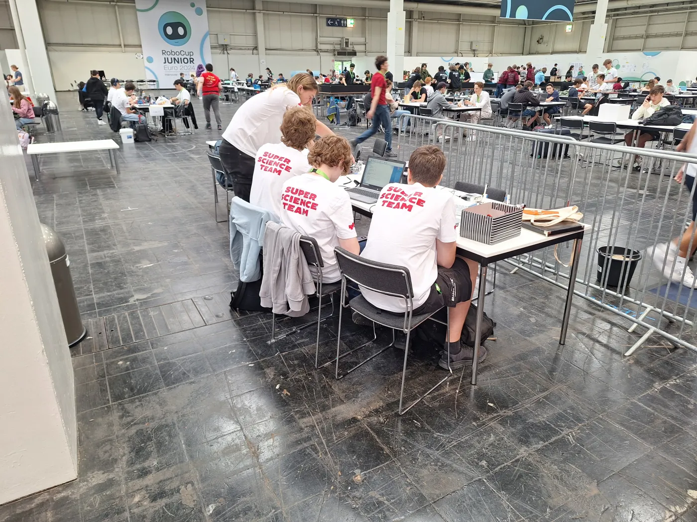 Das Team am Arbeiten. Man sieht die Teilnehmer von hinten (alle mit ihren Super-Science-Team-Shirts), wie sie gerade am Roboter bauen.