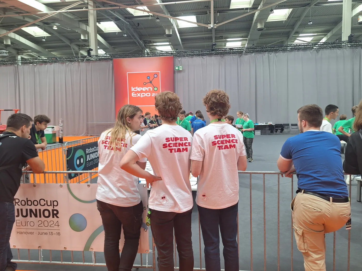 Das Team der AHS K&ouml;flach in ihren Super-Science-Team-Shirts. Man sieht 3 Team-Mitglieder von hinten, wie sie vor dem Wettbewerbsgel&auml;nde stehen.
