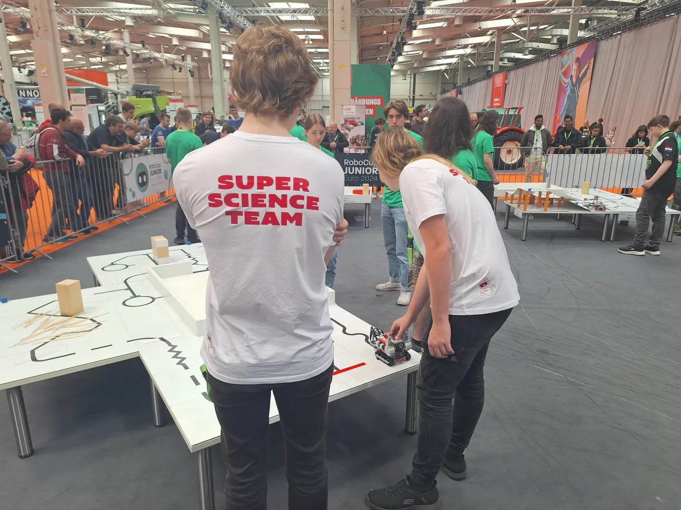 Das Team bei einer Probefahrt. Die Teilnehmer stehen vor einem wei&szlig;en Tisch mit schwarzen, aufgeklebten Linien. Man sieht einen kleinen Roboter, der den Linien entlangf&auml;hrt.