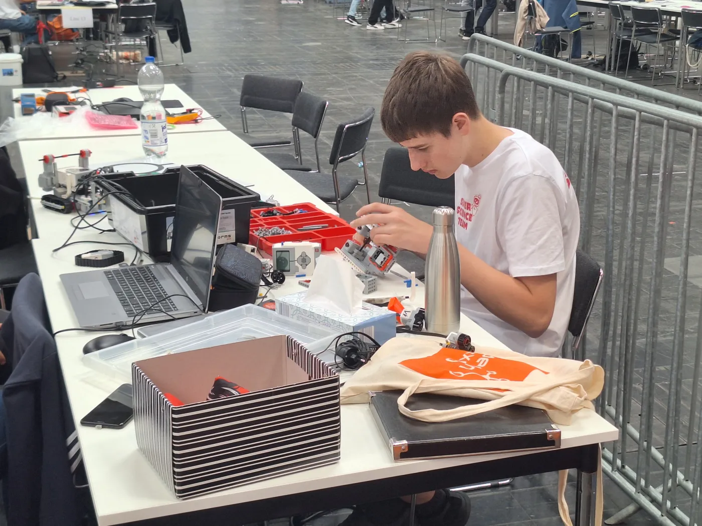 Ein Teilnehmer am T&uuml;fteln. Er sitzt an einem gro&szlig;en Tisch, der bedeckt ist mit Elektronikteilen und Computern und h&auml;lt gerade ein Teil des Roboters in der Hand.