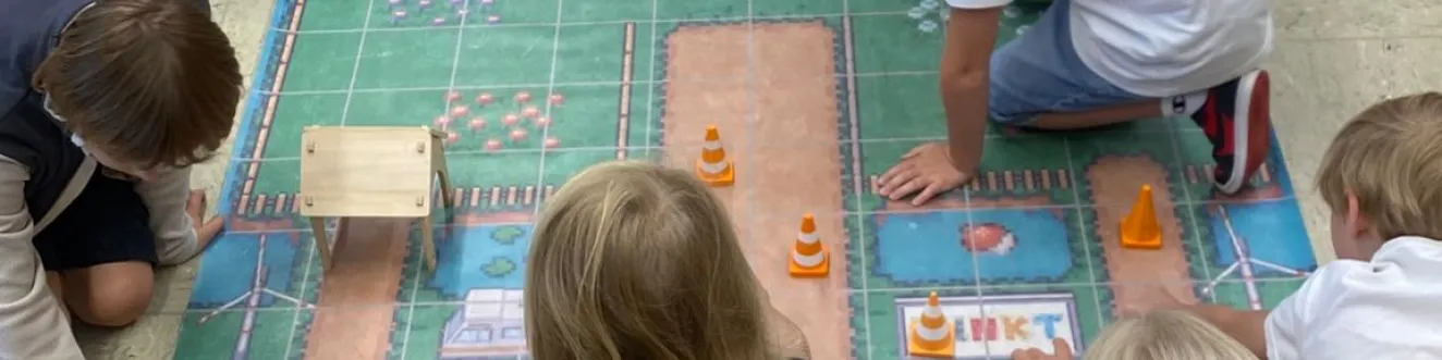 Eine Gruppe von Kindern spielt mit Spielzeugrobotern auf einem buntem Teppich.