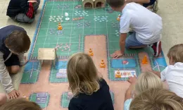 Eine Gruppe von Kindern spielt mit Spielzeugrobotern auf einem buntem Teppich.