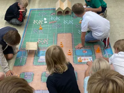 Eine Gruppe von Kindern spielt mit Spielzeugrobotern auf einem buntem Teppich.