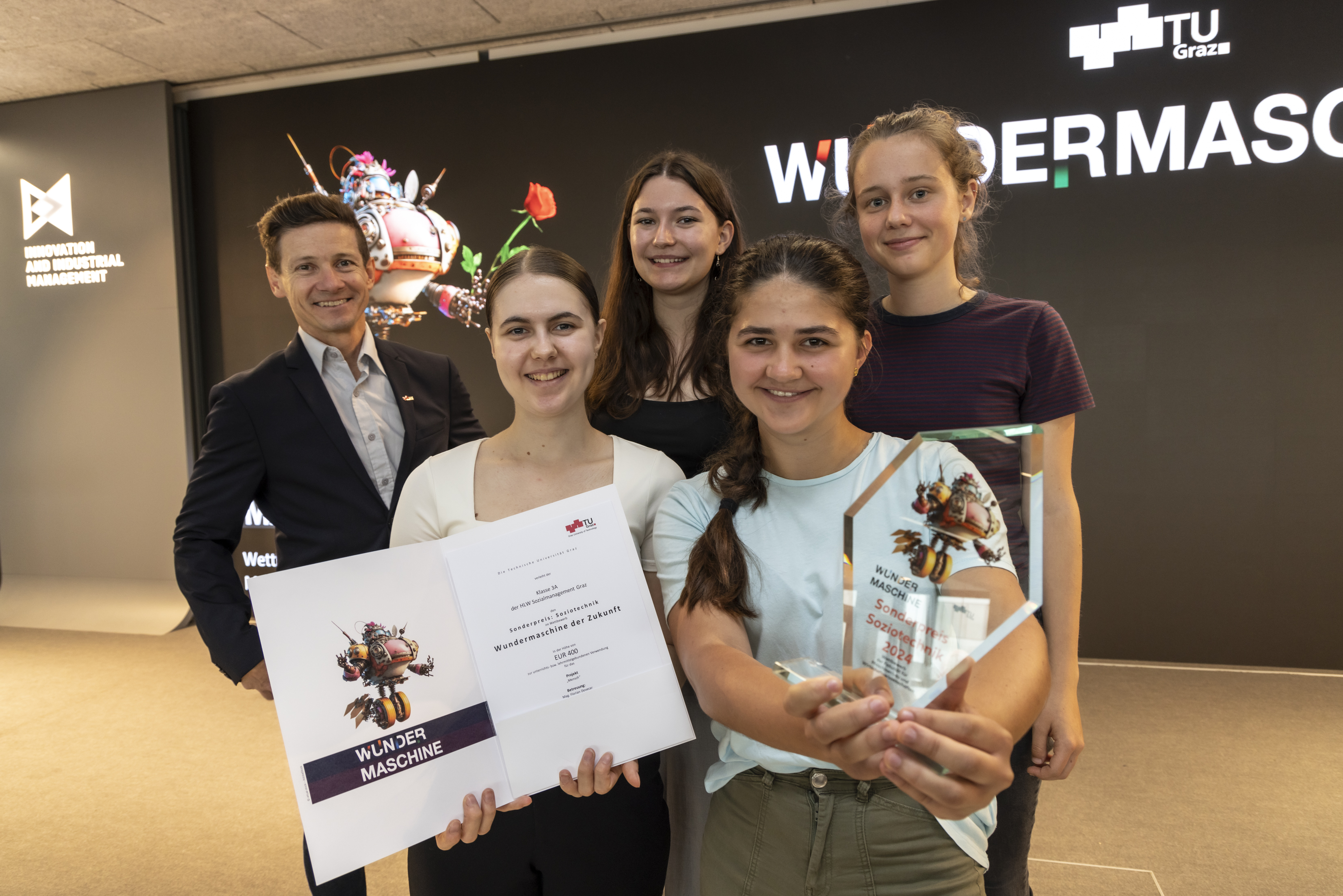 Vier Sch&uuml;lerinnen der Posieren stolz mit ihrer Urkunde und einem Pokal f&uuml;r den Sonderpreis des Wettbewerbs "Wundermaschine 2024"